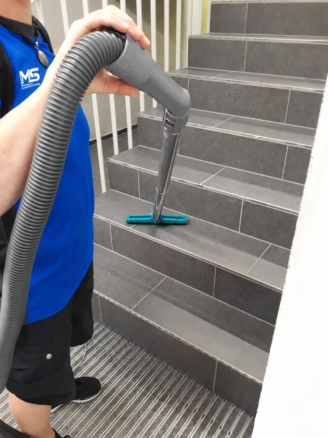 Treppenhausreinigung mit Staubsauger in blauer MSRH-Arbeitsbekleidung